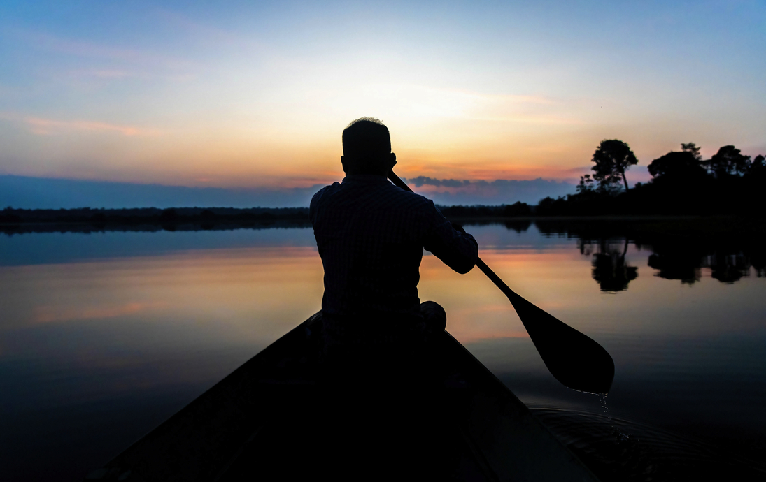 Silhouette eines Mannes, der in der Abenddämmerung auf ruhigem Wasser Kanu fährt - © PhotoSpirit - stock.adobe.com
